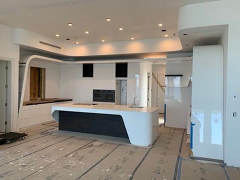 Open concept kitchen in progress with a curved white island and dark wood panel accent
