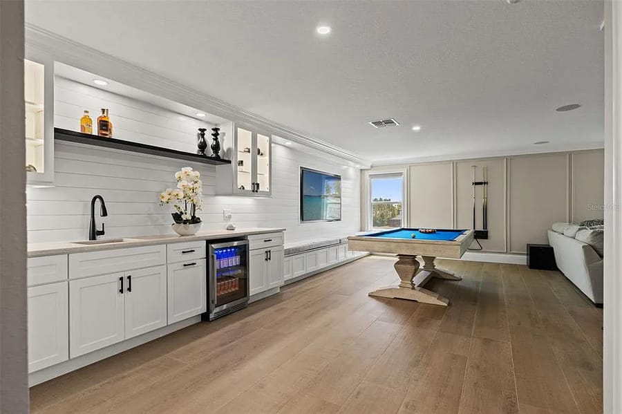 Wet bar with shiplap backsplash, open shelving and a game room beyond