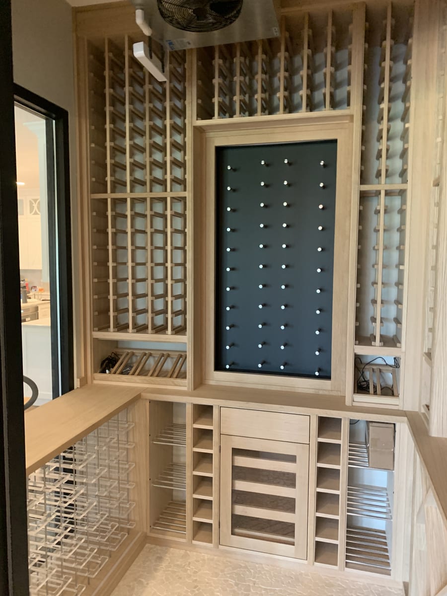 Wine cellar racking in raw oak with a lit pegboard bottle display panel