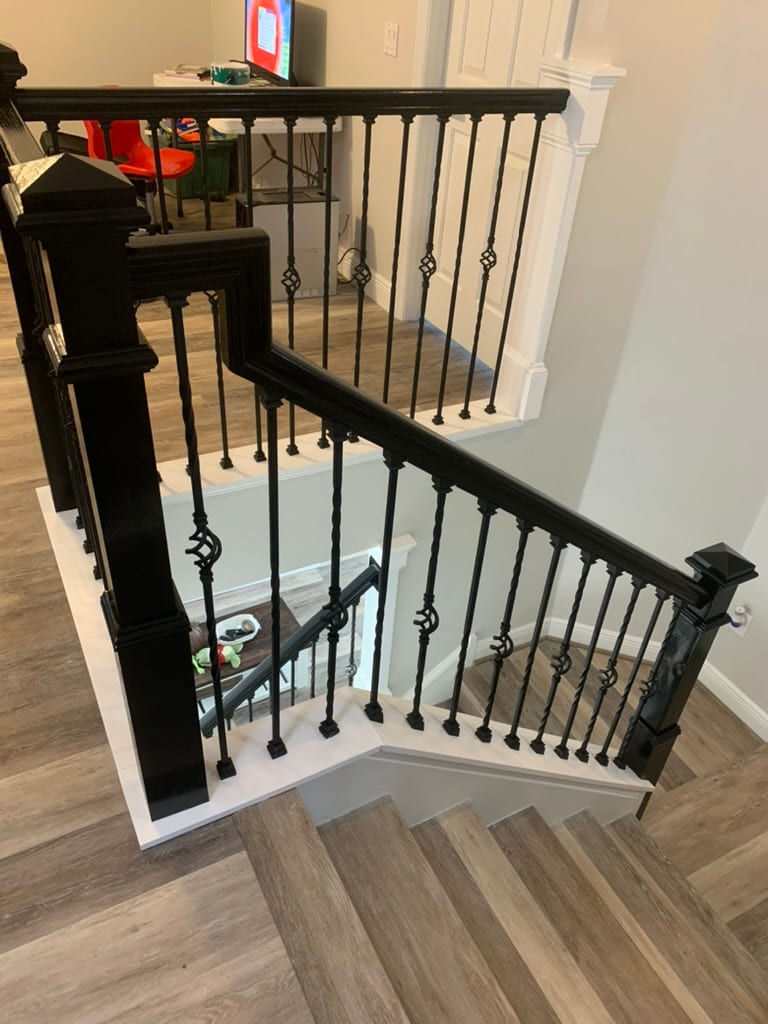 Corner stair landing with black iron balusters and a diamond medallion