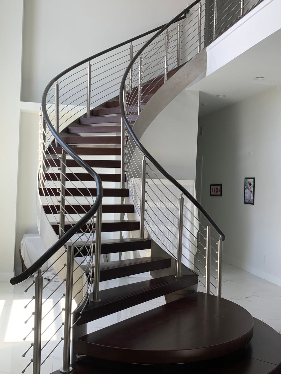 Curved staircase rising to a landing, dark treads and cable rail