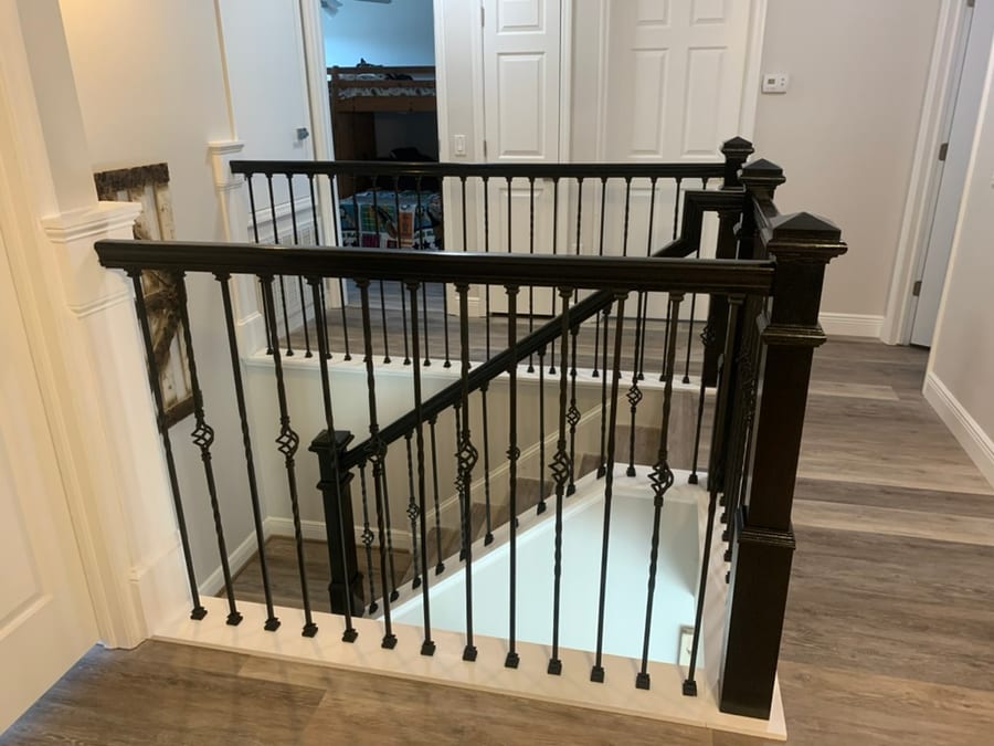Staircase landing overlooking a switchback stair, black iron balusters with diamond medallions