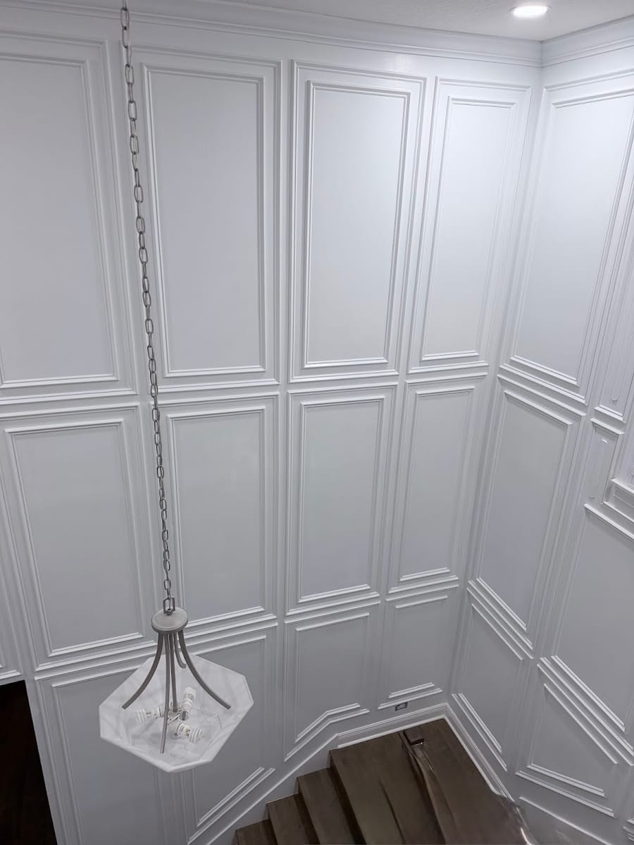 Full height raised panel wainscoting in a stairwell with a pendant chandelier