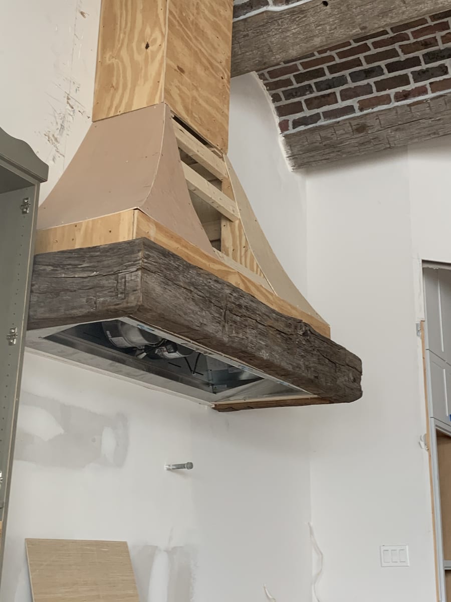 Custom range hood in progress, framed in plywood with a reclaimed wood beam mantel