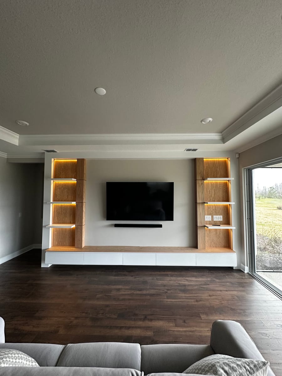 Floating oak wall unit with backlit shelving flanking a mounted television