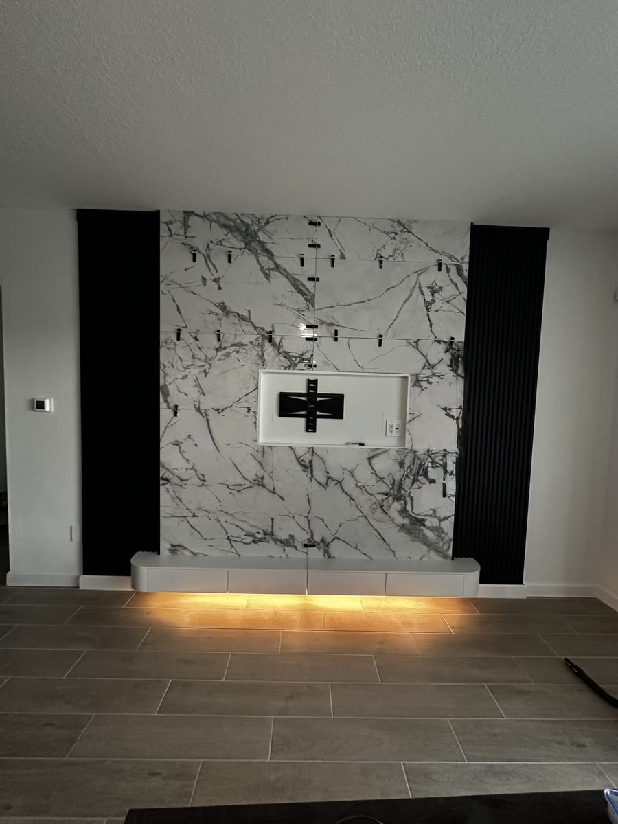 Marble slab TV wall flanked by black fluted panels, in progress